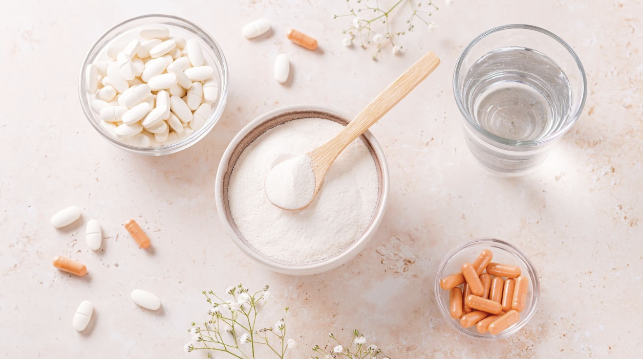桌面擺放著多種營養補充品,包括一碗白色粉末與木匙、兩小碗膠囊與錠劑、以及一杯清水,呈現健康管理的情境