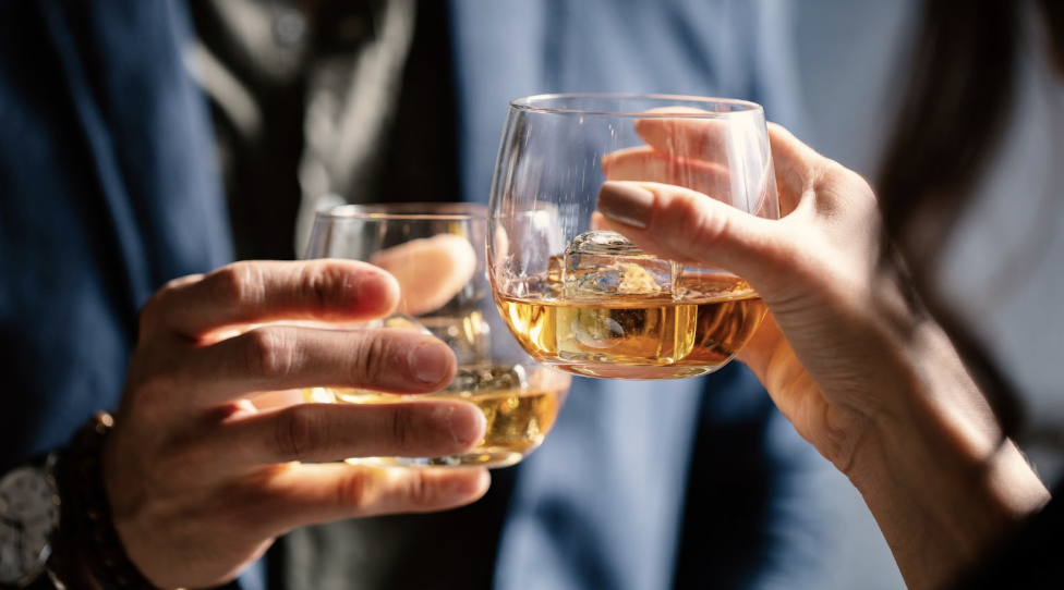 兩人舉杯碰杯飲用威士忌,近距離拍攝酒杯與琥珀色酒液