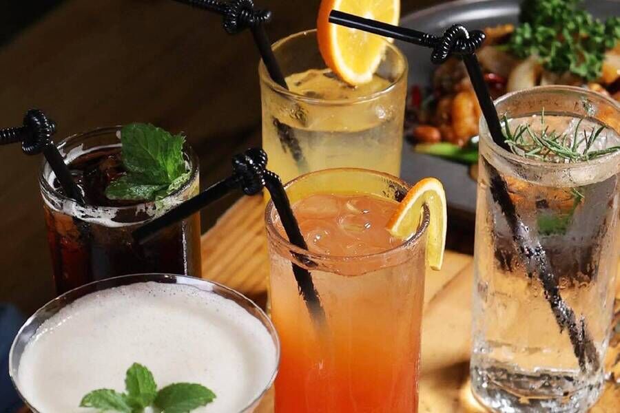 木桌上擺放多杯清涼調飲與氣泡飲，包含檸檬片裝飾的橘色漸層飲、透明氣泡水配迷迭香、深色可樂加薄荷，以及奶泡飲品，搭配黑色吸管與冰塊，呈現清爽消