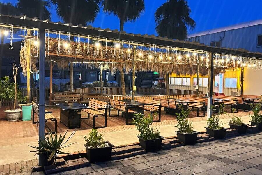 充滿南洋風情的戶外景觀餐廳，設有茅草屋簷、發光燈串及整齊的木質長椅用餐區