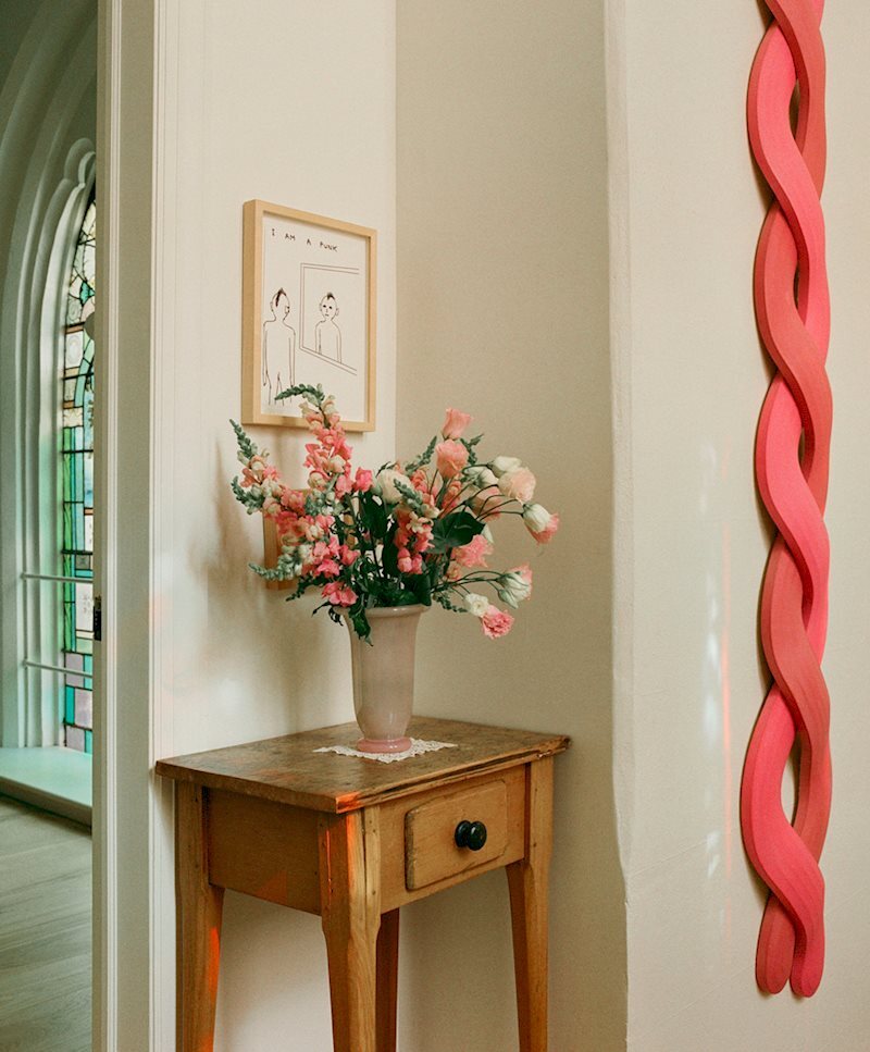 「同樣的東西驅動你拿起畫 布魯克林教堂改建宅邸走廊,HAY Empire 花瓶搭配鮮花,背景教堂彩繪玻璃窗與 Landon Metz 裝置作品