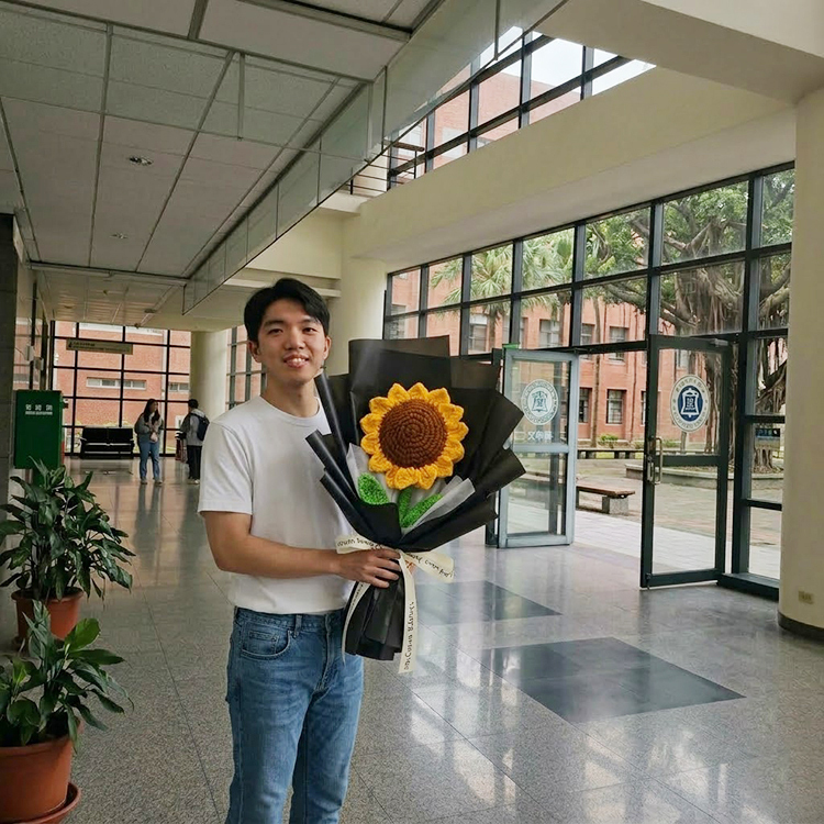 男大學生開心微笑手拿黑色包裝手作巨型編織向日葵花束在大學校園裡