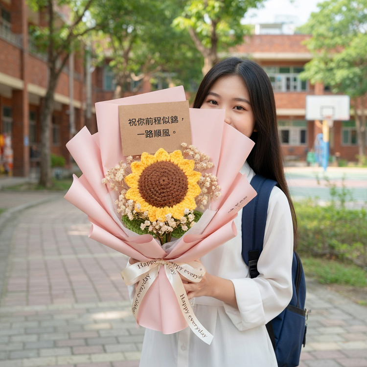 在充滿陽光的校園紅磚建築背景中，一名背著深藍色背包、穿著白色上衣的女學生雙手捧著巨大的手工編織向日葵花束。粉紅色包裝紙的花束上附有「祝你前程似錦，一路順風」的祝福卡片，展現出溫馨的畢業氛圍。