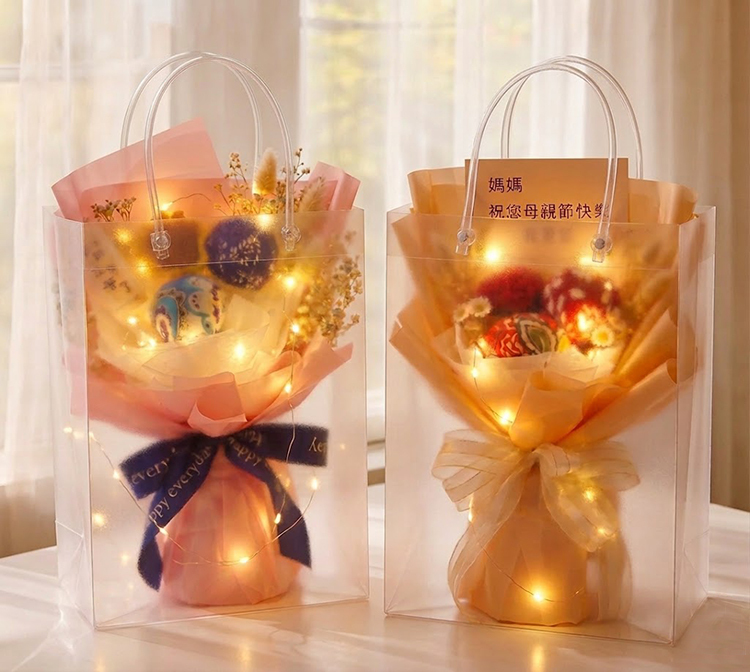 兩束艾草槌花束分別裝在半透明霧面立體提袋中，內部纏繞暖色 LED 燈串，營造出溫馨閃耀的禮品感。