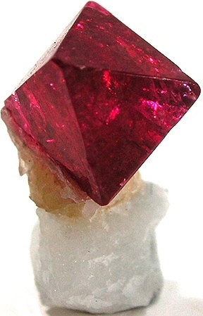 Natural octahedral red spinel crystal on a white matrix, showing sharp geometric faces and vivid deep red color.