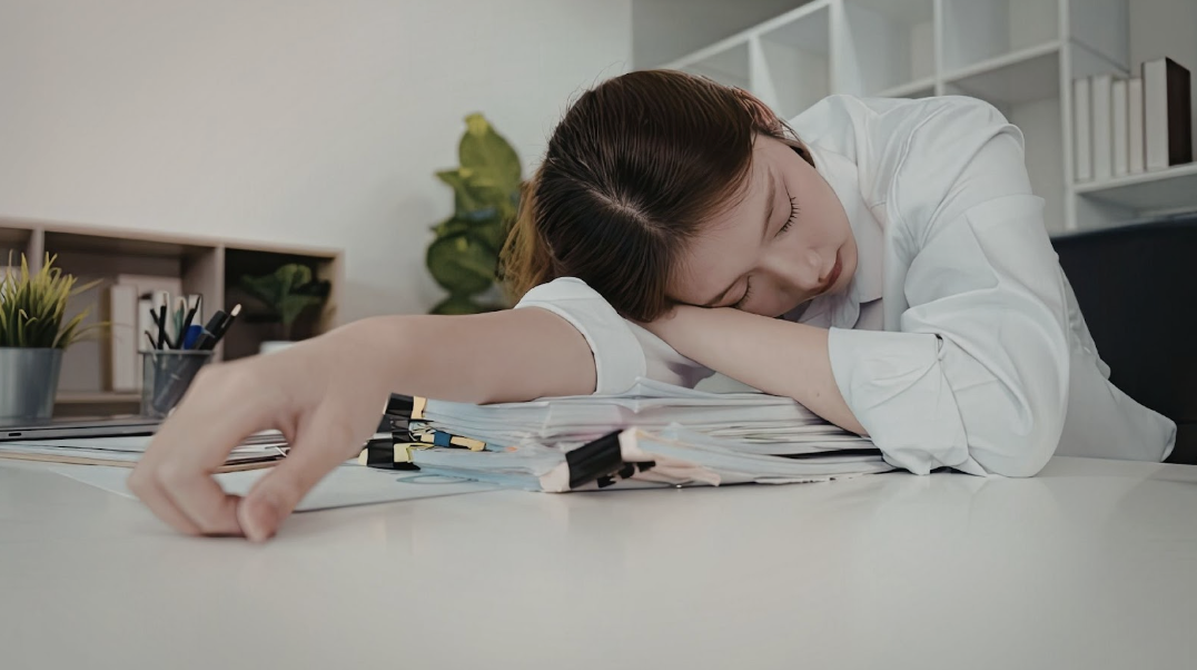 辦公室女性因疲累趴在文件堆上休息,呈現職場壓力與過度勞累的情境