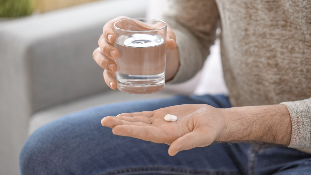 男子手心放著兩顆白色藥錠,另一手拿著水杯,準備服用保健食品或藥物