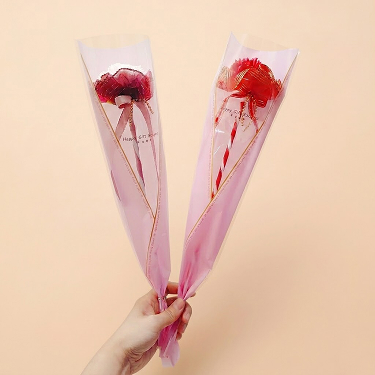 兩支單支包裝的香皂康乃馨花束，分別為深紅色與鮮紅色，配有粉色透明包裝紙與蝴蝶結