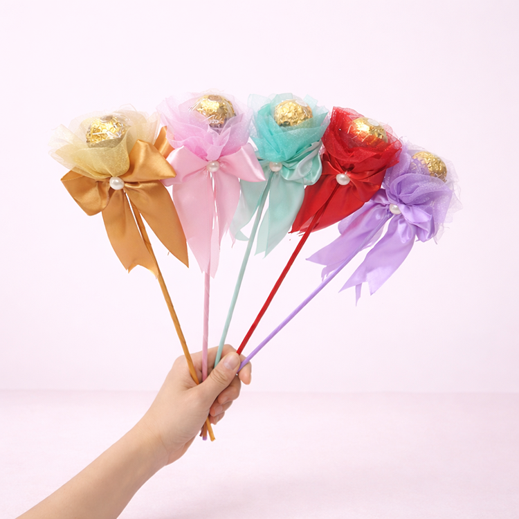 五色金莎花束展示圖,一隻手拿著金色、粉紅、薄荷綠、紅色與紫色單枝金莎棒棒花,搭配緞帶與珍珠裝飾,背景為柔和淺粉色 #FDEBED。適合母親節禮物、情人節禮物、畢業禮物、小禮物、金莎花束商品圖。
