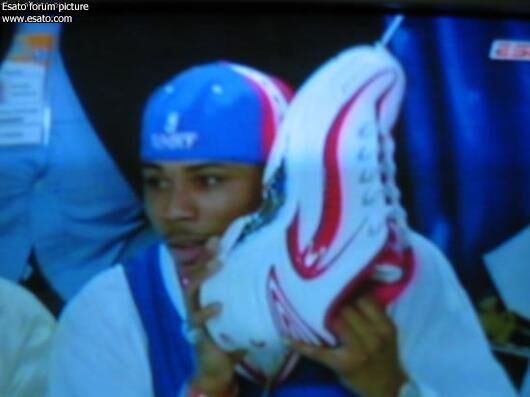 2005 年 NBA 全明星週末畫面截圖，俠客歐尼爾手持一隻內嵌手機的特製巨大球鞋亮相，呼應其一貫的搞怪風格，也是日後聯名鞋款內嵌可樂罐創意的早期預兆。