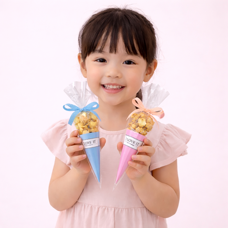 小女孩笑容燦爛地展示粉藍與粉嫩色系的「愛的爆爆」爆米花甜筒，溫馨可愛的氛圍，適合幼兒園生日派對、兒童節活動與周歲派對小禮物。
