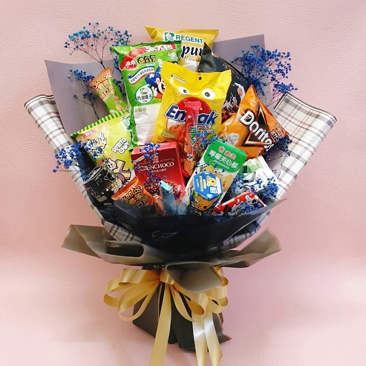 一束裝滿各種知名品牌零食（如多力多滋、巧克力）的創意花束，採用黑色與格紋包裝紙及金色緞帶裝飾，背景為簡約粉色質感背景。