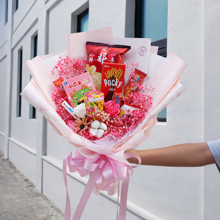 手拿粉色包裝的零食花束,背景為白牆白窗