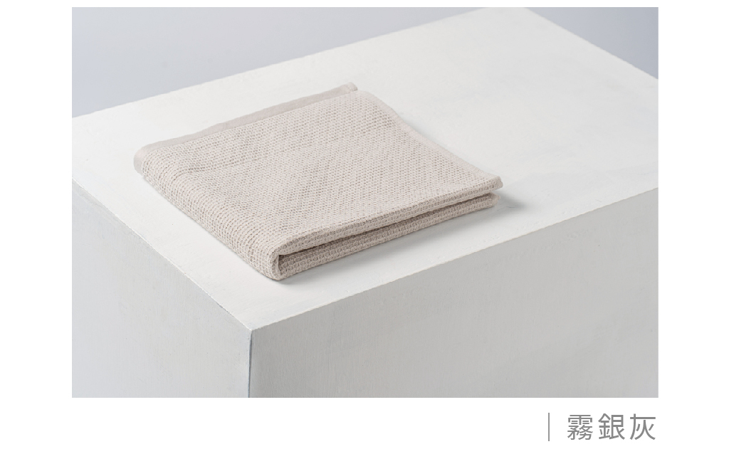 HEXA 快乾系列毛巾顏色展示圖。呈現「霧銀灰」款式實體顏色，毛巾平摺放置於白色幾何展示台上。