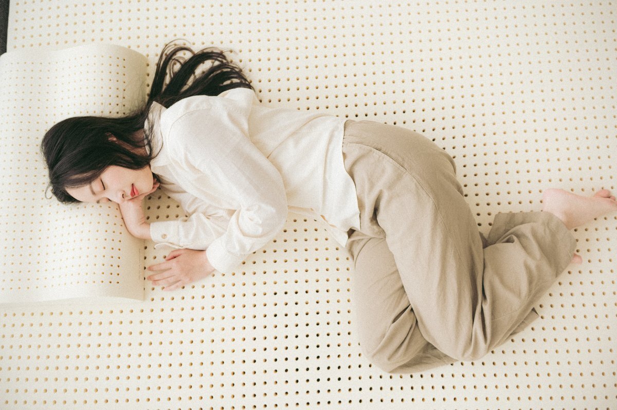 女性側睡在天然乳膠床墊上俯拍，展現乳膠透氣孔洞與貼合支撐效果