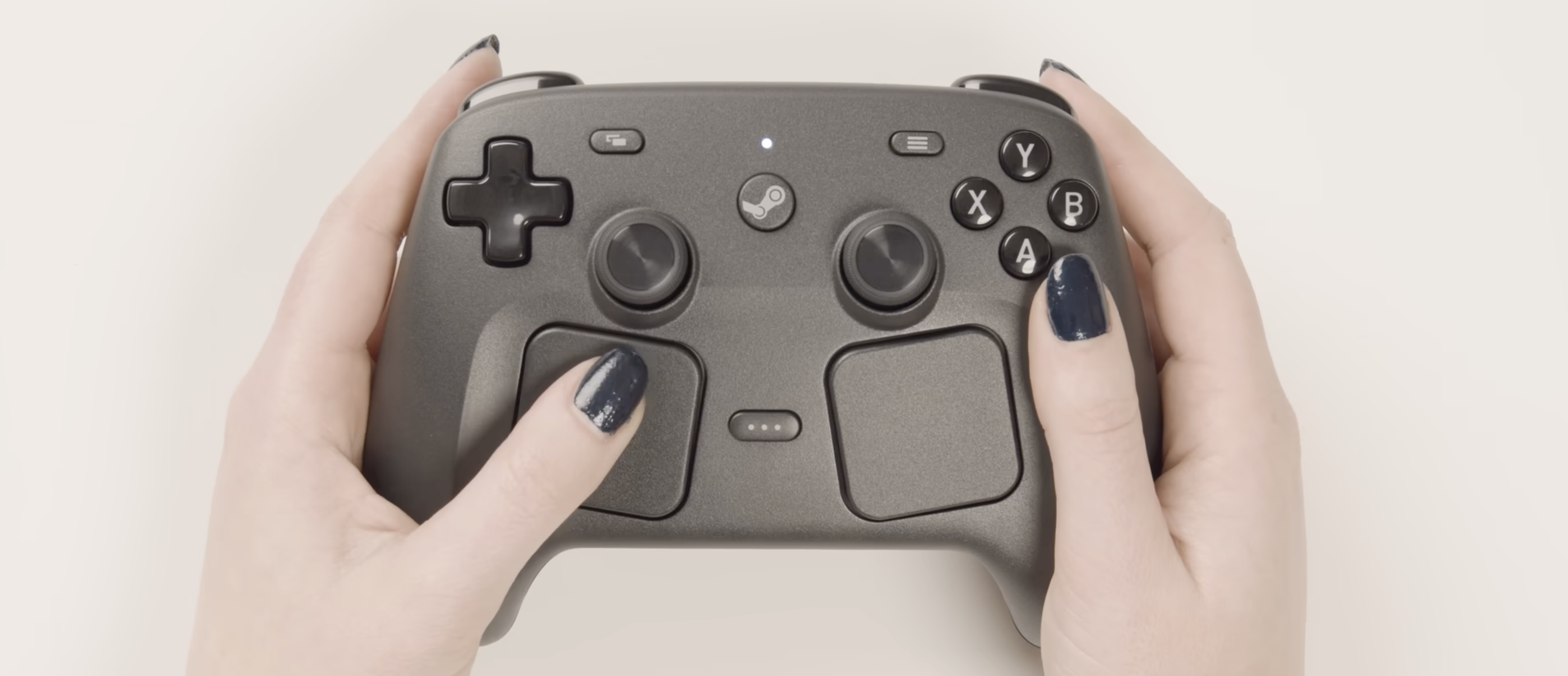 Steam Controller 2 代正面握持俯視特寫，深灰色機身清晰呈現雙搖桿、D-Pad、ABXY 按鍵、Steam Logo 中央鍵與下方左右兩片方形觸控板配置，拇指正點觸左側觸控板。