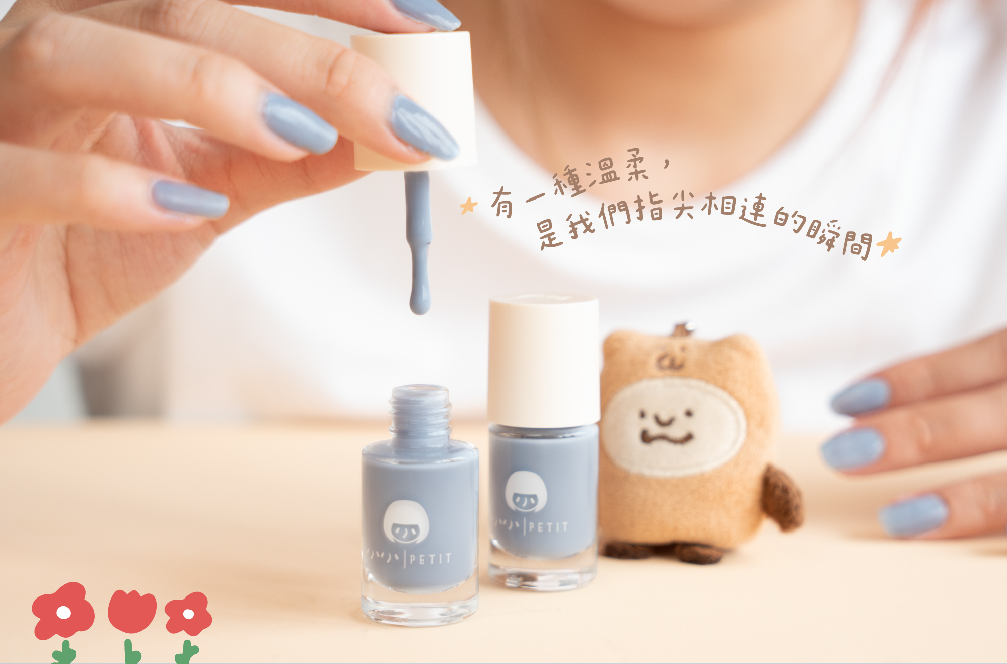 小小PETIT × 咻咻熊聯名指甲油「懶懶時光」暖藍色系，女性手持指甲油瓶，指尖塗有療癒暖藍色水性無毒指彩，旁邊擺放咻咻熊小小薯泥布偶吊飾，呈現「有一種溫柔，是我們指尖相連的瞬間」聯名主視覺。