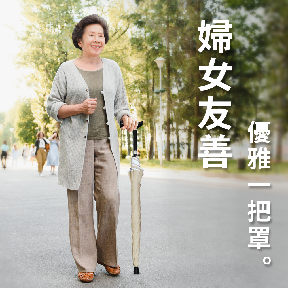 一位面帶微笑的婦女穿著灰色針織外套,優雅地在樹木滿布的公園步道上散步,手中撐著一把米白色的登山輔助傘