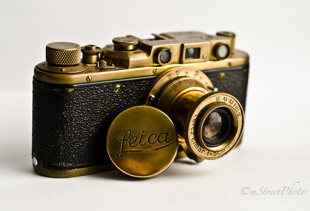 復古黃銅色 Leica 古董相機,黑色蛇紋皮革機身搭配金色鏡頭蓋與 Leitz Elmar 鏡頭,呈現經典機械相機質感。復古黃銅色 Leica 古董相機,黑色蛇紋皮革機身搭配金色鏡頭蓋與 Leitz Elmar 鏡頭,呈現經典機械相機質感。