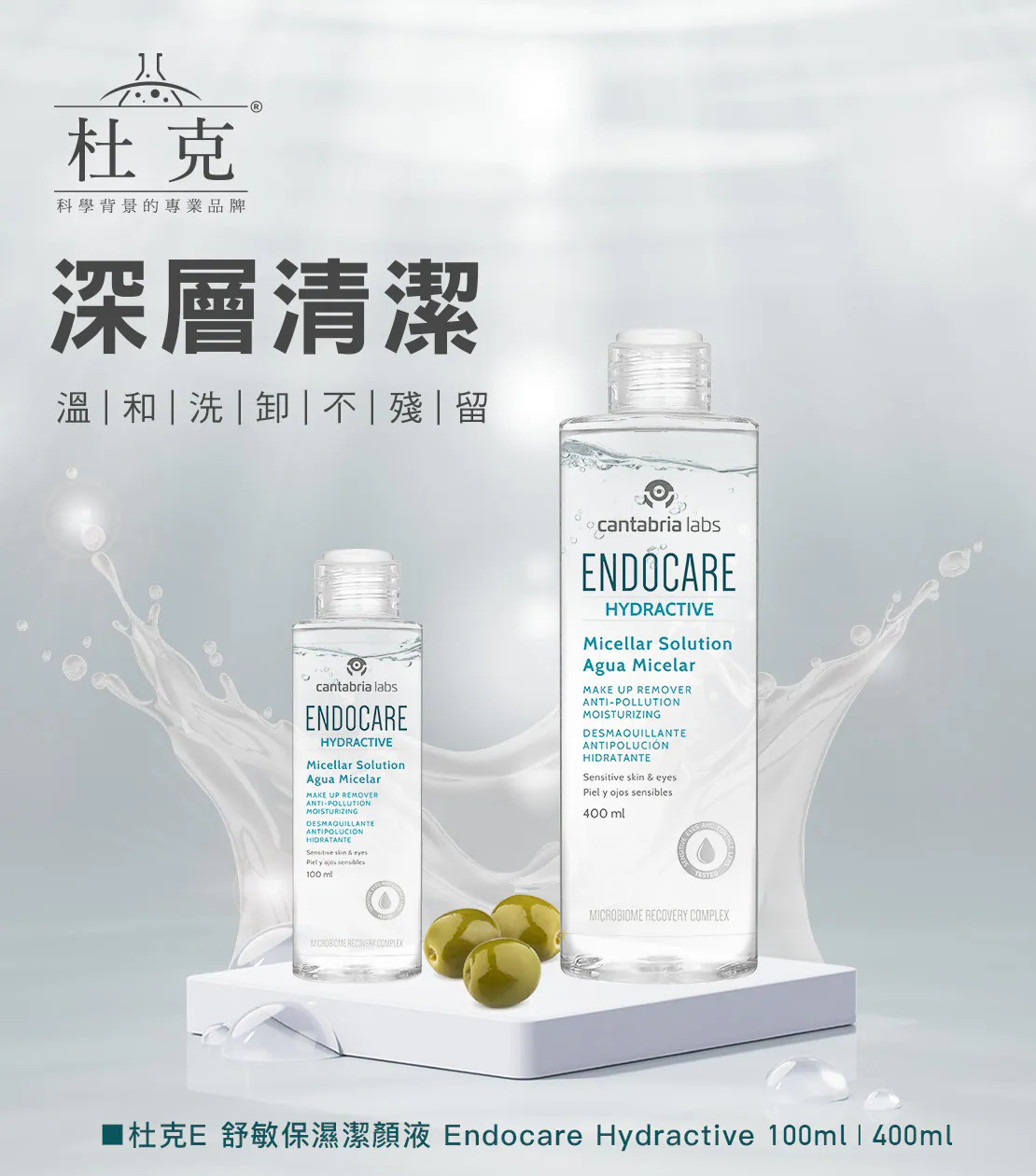 這是杜克 E「舒敏保濕潔顏液 (Endocare Hydractive)」的宣傳圖。畫面展示了 100ml 與 400ml 兩種容量的透明瓶身產品,放置在白色方形平台上,旁邊點綴著幾顆綠色橄欖。背景為淺灰色,並有動態的水花濺起特效。左上方印有杜克 Logo 與主標題「深層清潔 溫 | 和 | 洗 | 卸 | 不 | 殘 | 留」。最下方標示完整中文品名與兩種容量規格