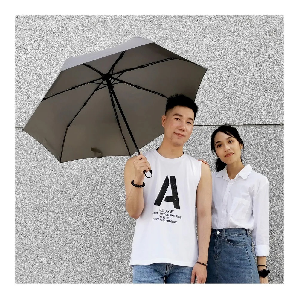 一對男女並肩站在灰色石子牆前,手持一把撐開的灰色自動折疊傘遮陽
