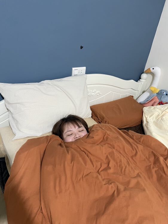 LOVEFU 大島樂眠冰島樂眠床使用者實拍:使用者蓋著棕色被子躺在冰島樂眠床上,露出滿足的笑容