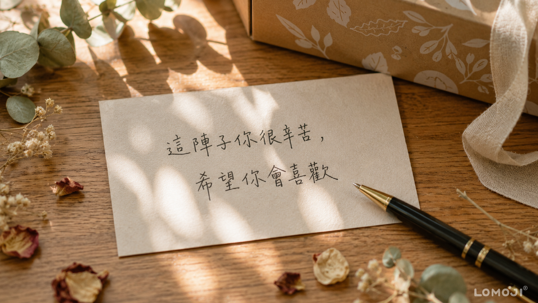 Alt 文字: 送禮手寫卡片包裝技巧特寫:木桌上擺放寫有「這陣子你很辛苦,希望你會喜歡」手寫字樣的卡片,旁邊附有鋼筆與樂木集足浴禮盒