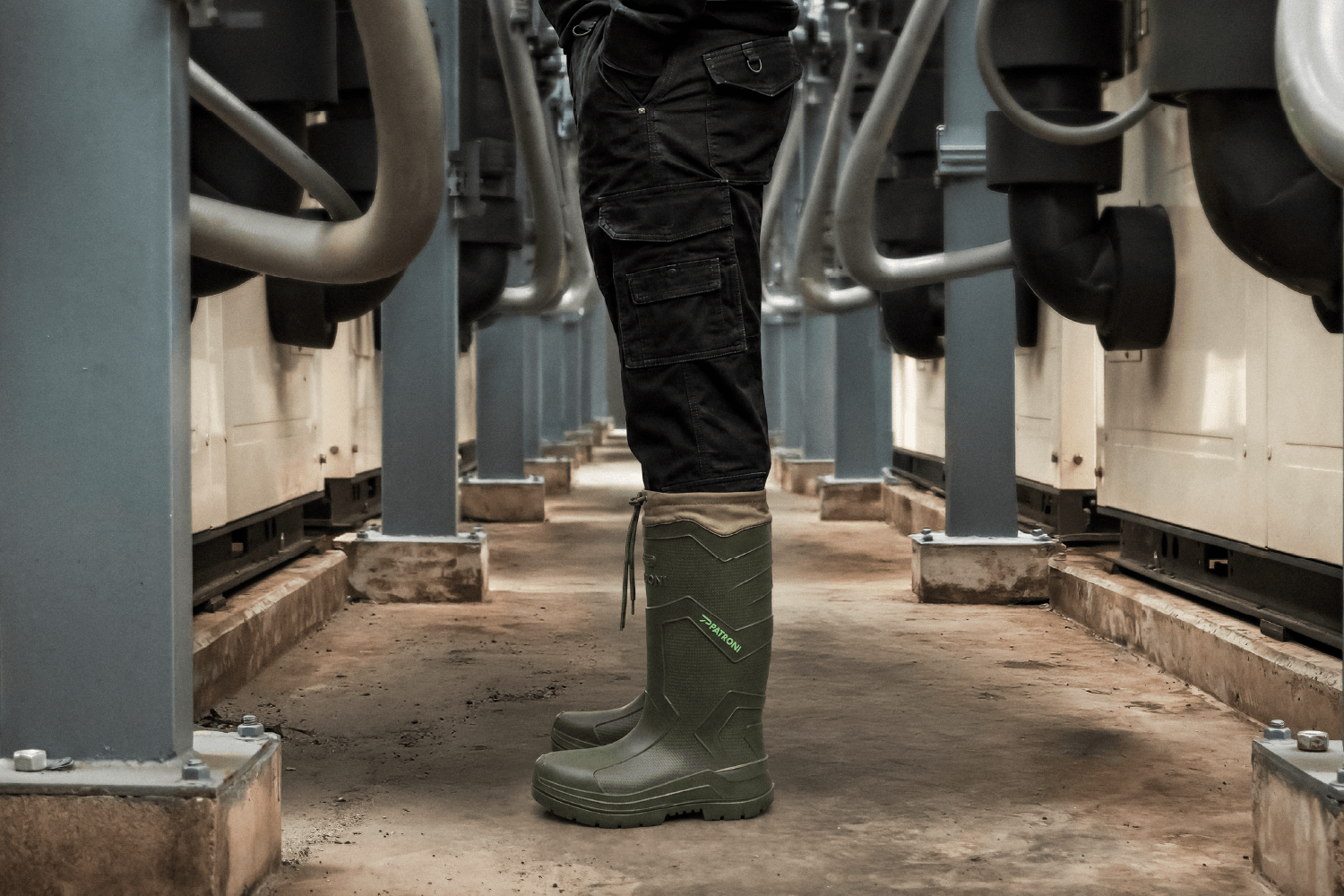 A worker in PATRONI SF2380DGN ultra-lightweight ladder-grip insulated safety rain boots, in a heavy industrial machine room