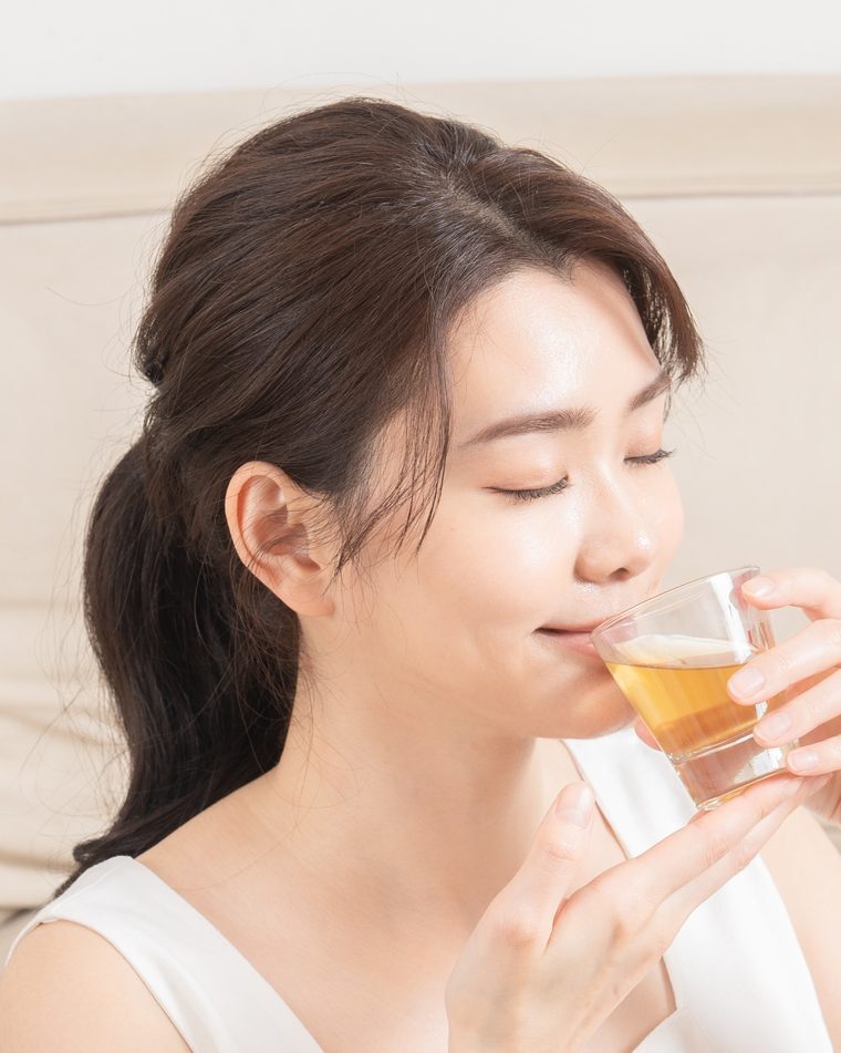 閉眼捧著玻璃杯喝養生茶的特寫