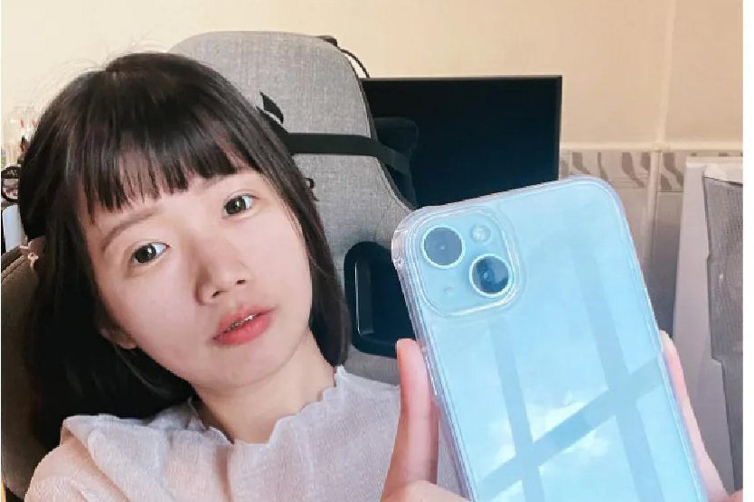 亭秝在室內手持裝上極地冰岩殼的 iPhone，透明殼面反射窗外光線