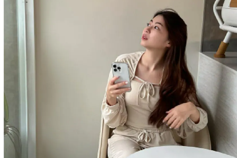 Ki媽拎兒日記坐在窗邊，手持裝上極地冰岩殼的 iPhone