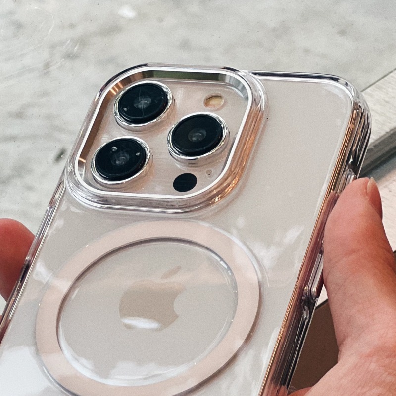 手持透明明岳殼 iPhone，鏡頭外圈的金屬鏡框與背面磁環清晰可見