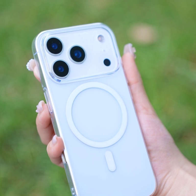 手持零手感 Lite Case 包覆的白色 iPhone，殼身高度通透，背面 MagSafe 磁環清晰，背景為草地