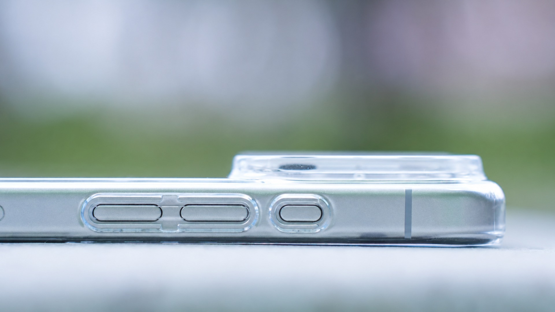 零手感 Lite Case 包覆的 iPhone 橫躺於淺色檯面，殼壁極薄，側邊按鍵與鏡頭外圈開孔清晰可見