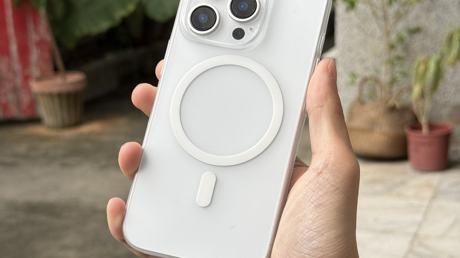 手持白色 Air Lite Case 磨砂超薄殼的 iPhone 於戶外植栽前，霧面殼身不反光