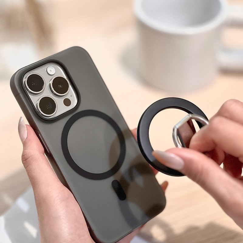 手持黑色磨砂超薄殼的 iPhone，另一手將 MagSafe 磁吸環靠上背面磁圈