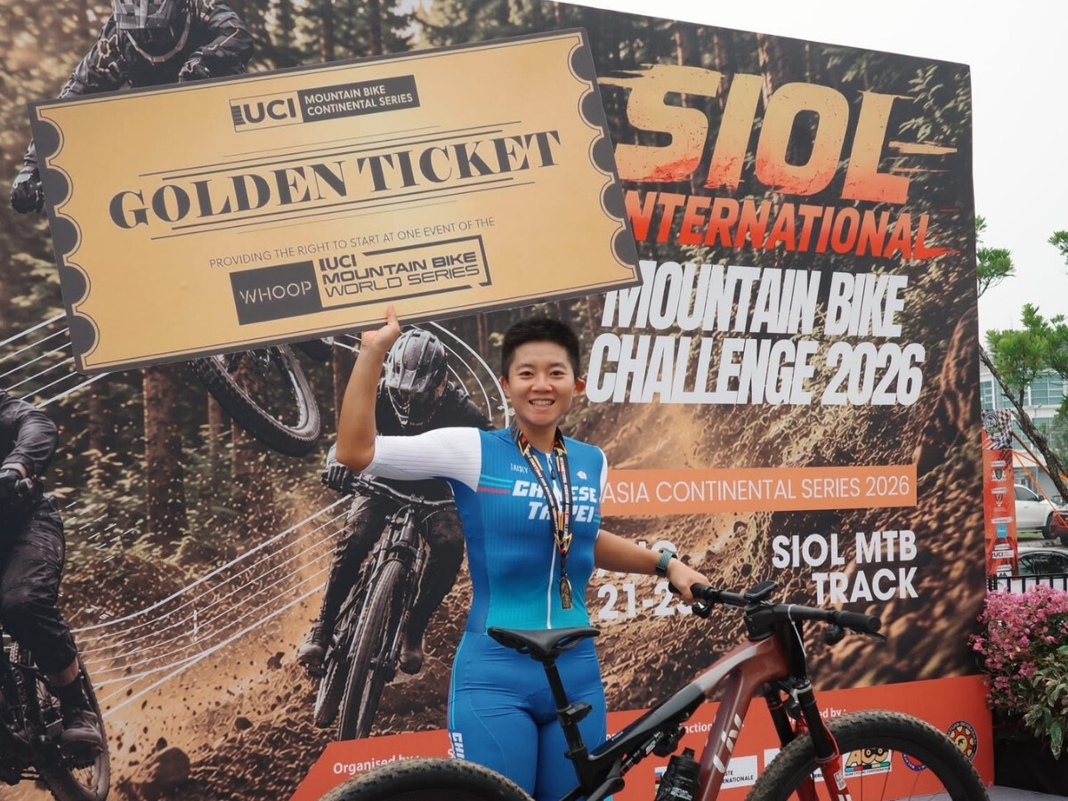 台灣登山車選手蔡雅羽手持 UCI 世界盃 Golden Ticket 於 2026 洲際系列賽頒獎牆前合照