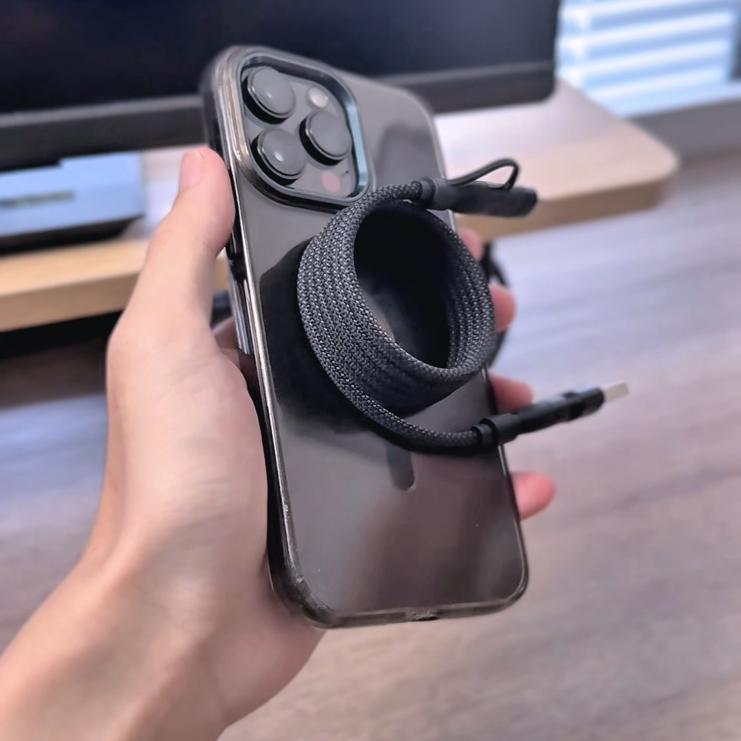手持 iPhone，磁吸四合一快充線捲收成圈靠在機身旁，線身可見編織紋理