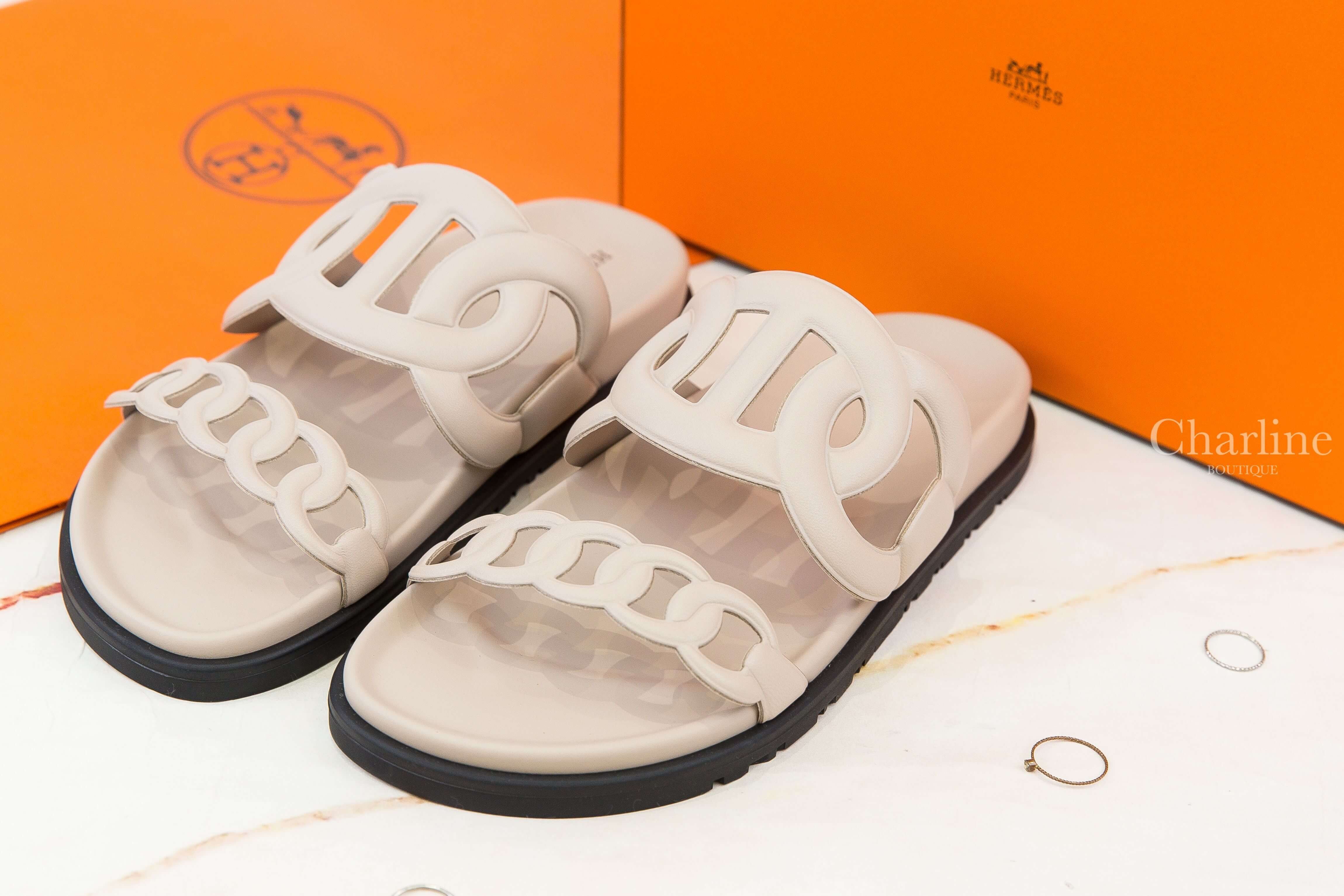 Hermès Extra Sandal 米色θ黑底小牛皮平底拖鞋 正面成雙展示，米色小牛皮雙鞋帶搭配鏤空H造型與黑色鞋底