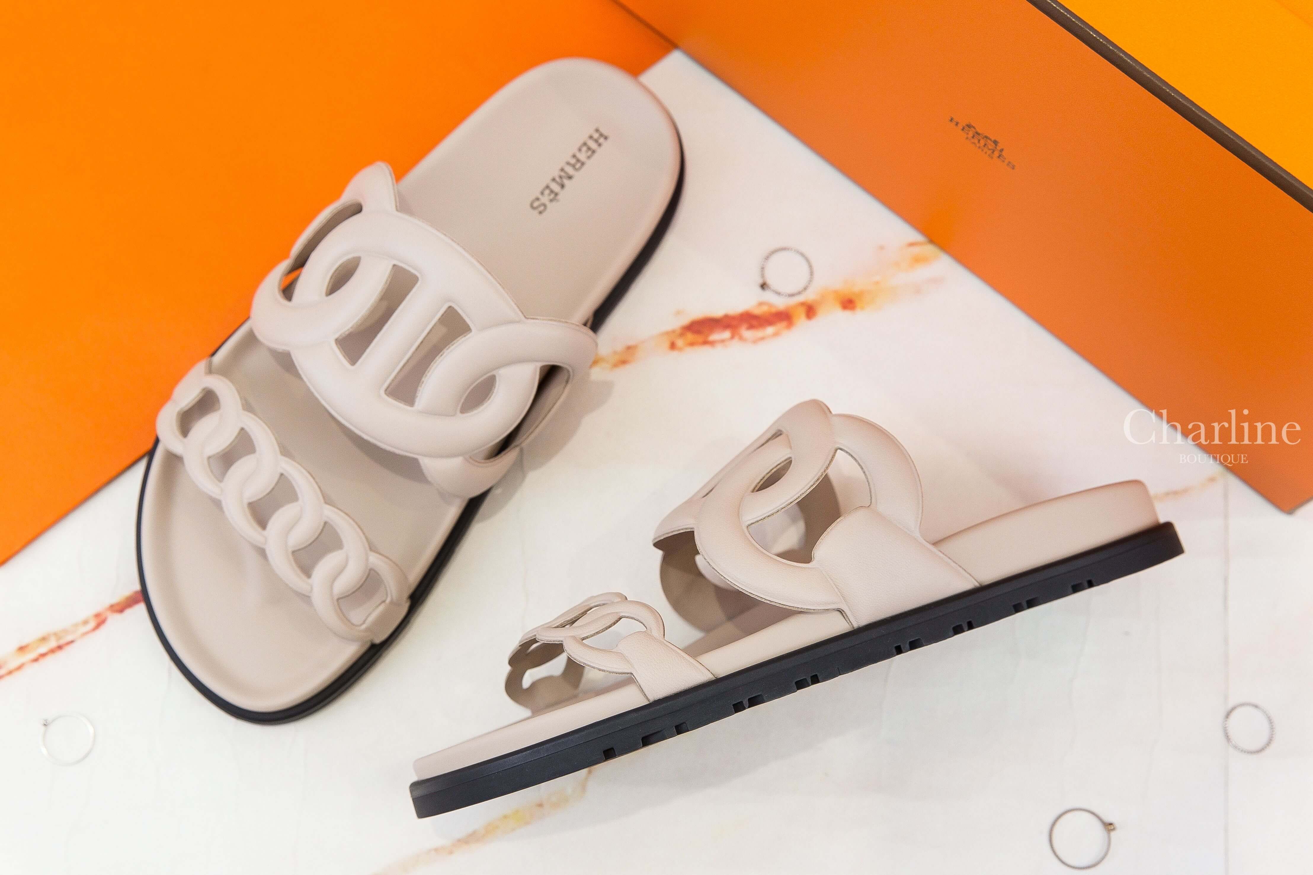 Hermès Extra Sandal 米色θ黑底小牛皮平底拖鞋 側面角度展示，呈現雙鞋帶鏤空設計、平底輪廓與黑色鞋底