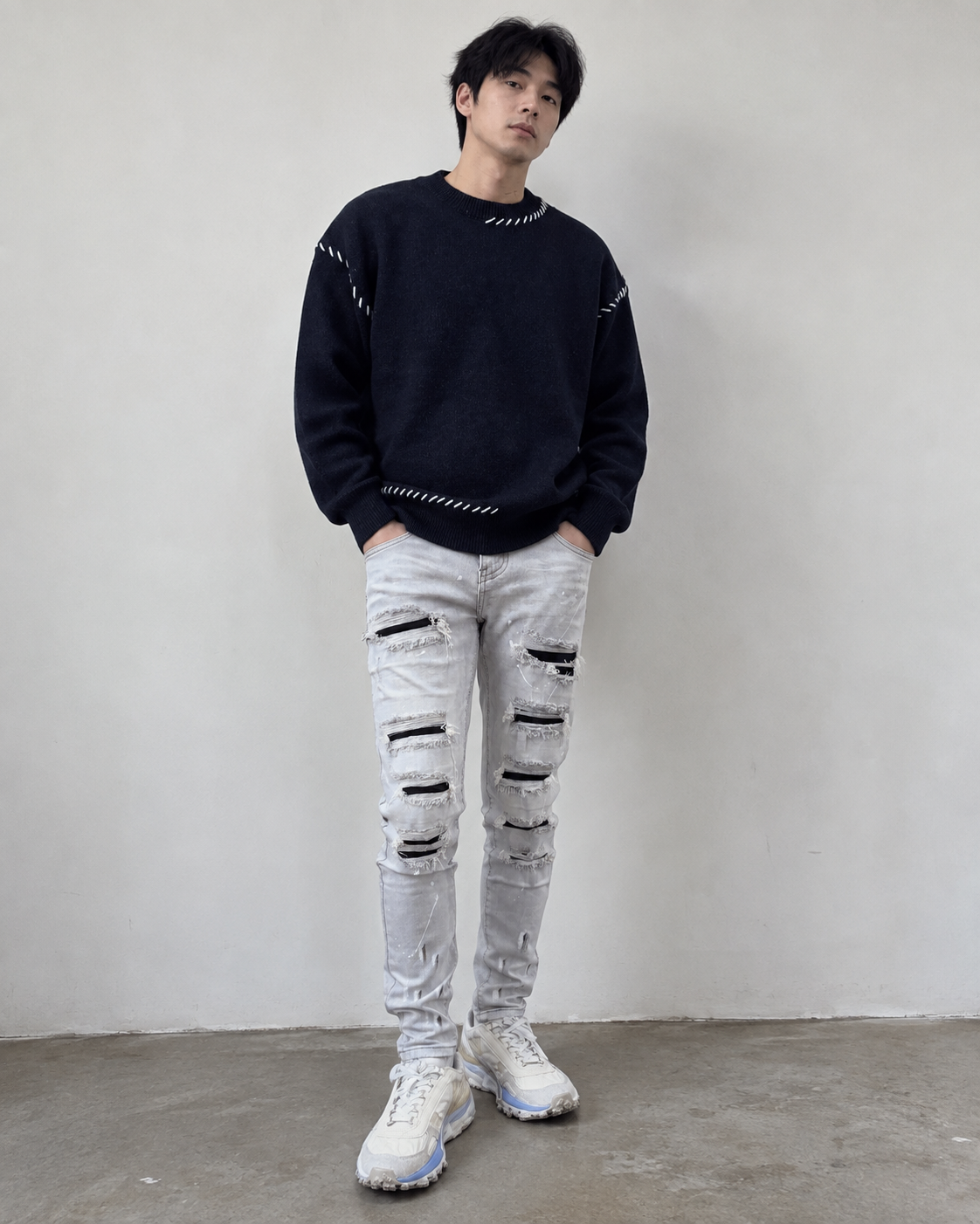 深藍色白線細節針織毛衣搭配淺灰色破壞牛仔褲的男生穿搭