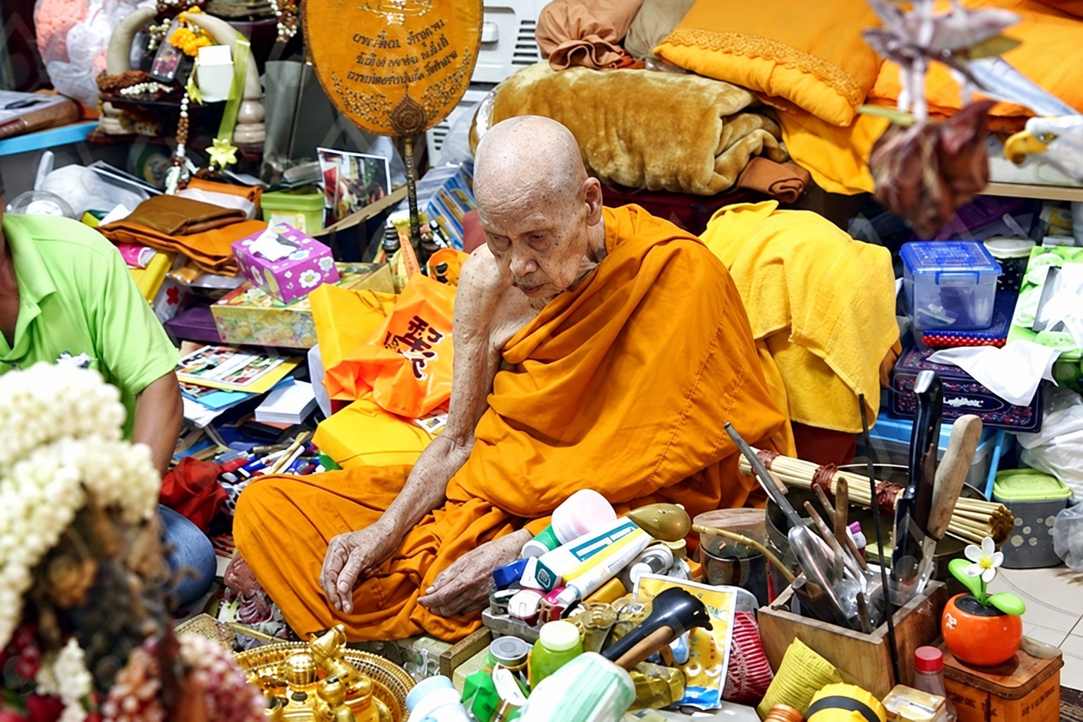一位泰國僧人坐在供奉物與日常器物之間