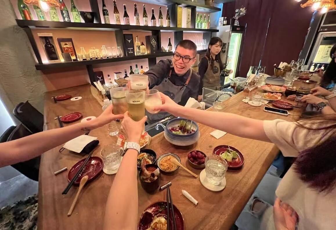 酒桃店內吧台前眾人舉杯互動的場景