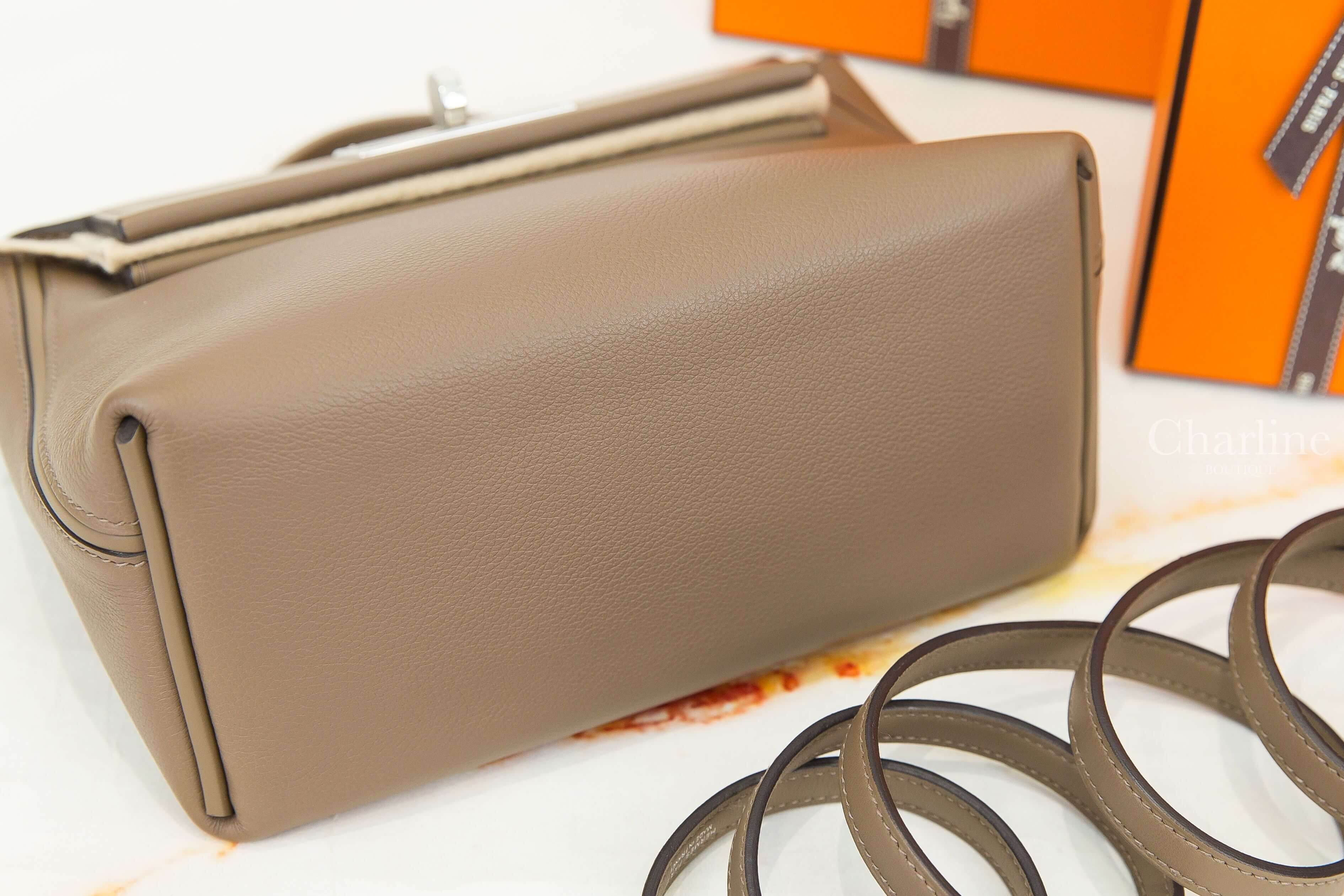 Hermès Mini Kelly 2 大象灰手提肩背包底部斜角特寫，展示平整皮革包底、側邊摺角結構及包身皮革紋理，旁邊擺放同色長肩帶。