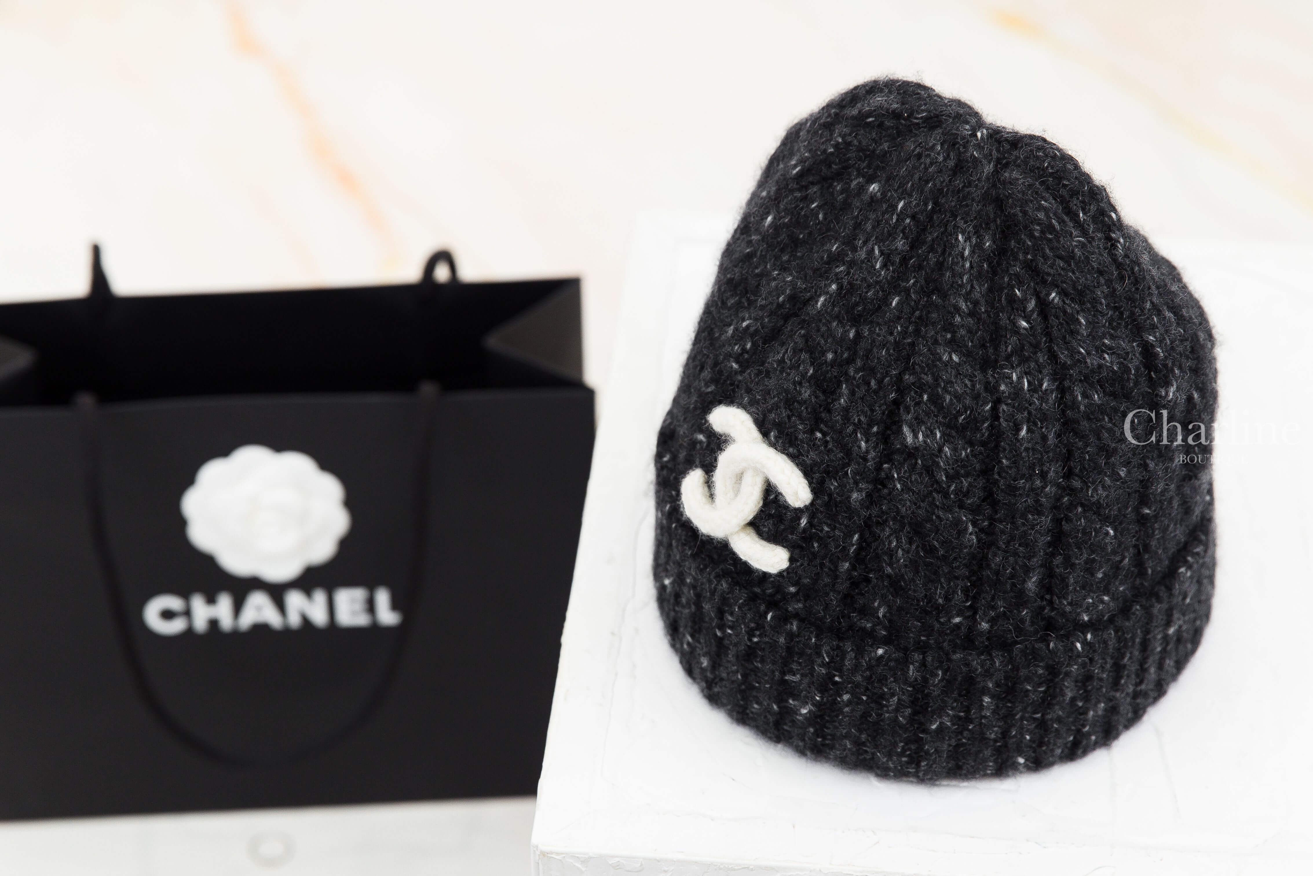 CHANEL 香奈兒黑色白雪花針織毛帽左前側展示，細看帽頂收針結構、黑色混白紗線與立體羅紋編織，白色雙 C 標誌位於反摺帽沿側前方。