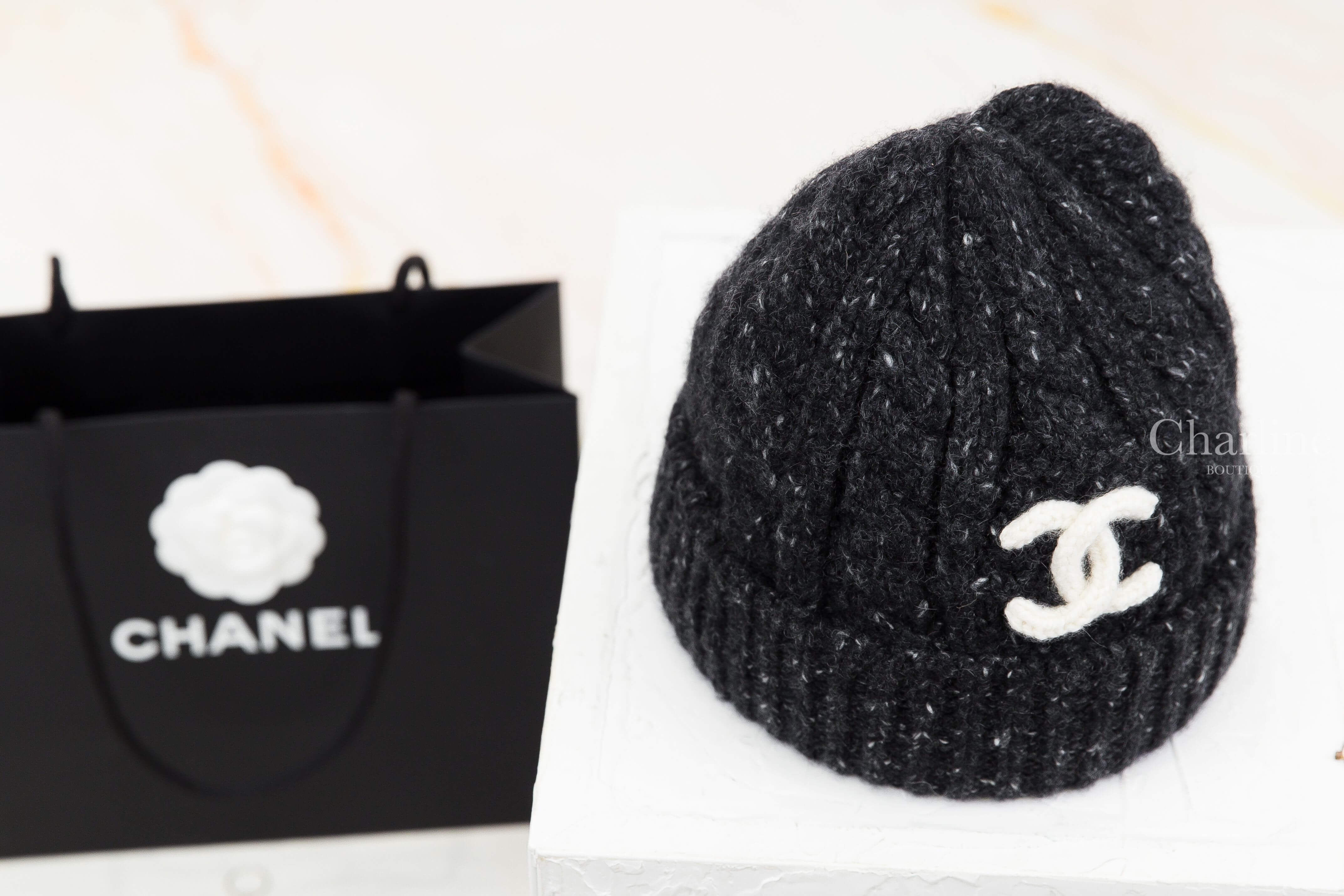 CHANEL 香奈兒黑色喀什米爾毛帽右前側斜角展示，呈現圓弧帽型、立體針織紋路與反摺帽沿，白色雙 C Logo 位於帽身前側，展現黑白配色設計。