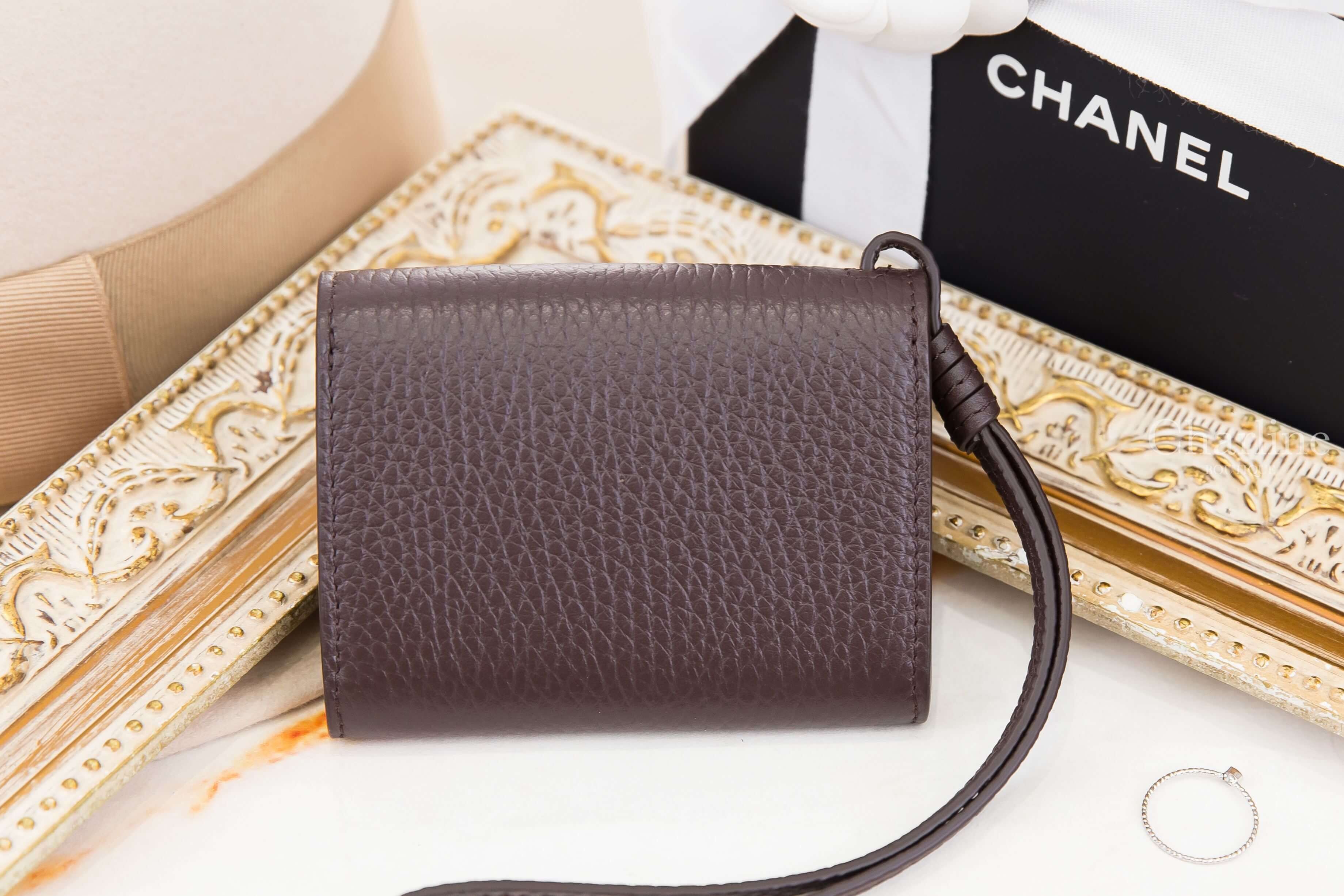 Chanel Mini Bag Charm 深棕色粒紋小牛皮卡片零錢夾背面展示，搭配皮革腕帶與CHANEL品牌包裝