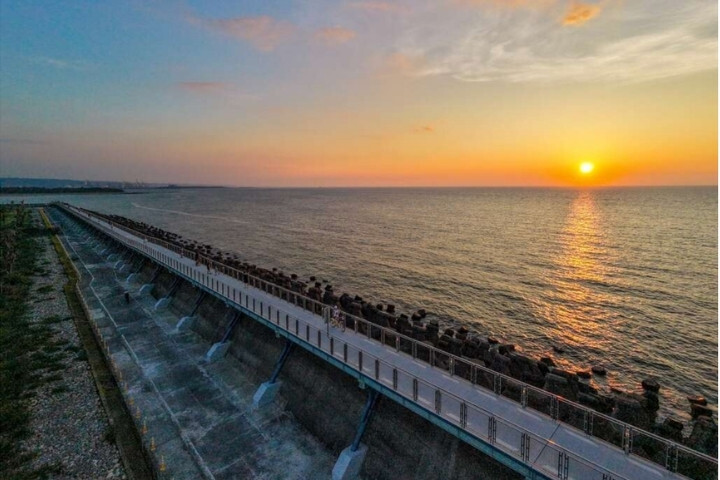 淡水金色水岸觀海長堤自行車道,夕陽映照海面,堤頂自行車道沿著海岸延伸。